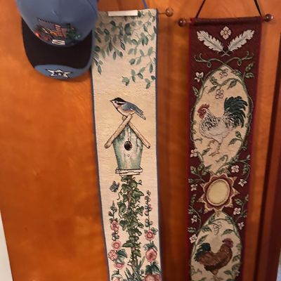 Sale Photo Thumbnail #106: Pair of narrow woven tapestry wall hangings featuring bird house and rooster motifs alongside a light blue baseball cap.