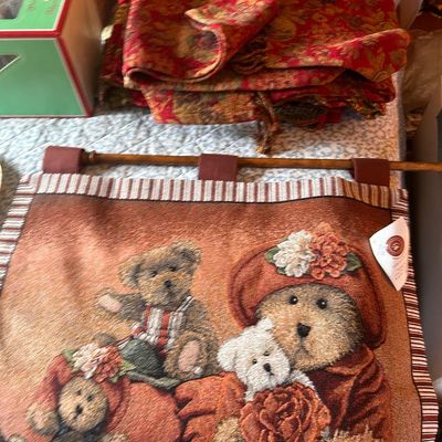 Sale Photo Thumbnail #99: Woven tapestry wall hanging featuring a teddy bear motif on a wooden rod, alongside folded red and gold brocade fabric.