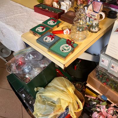Sale Photo Thumbnail #34: Collection of holiday decor and knick-knacks, including boxed silver-tone ornaments, glass tree jars, ceramic figurines, and string lights.