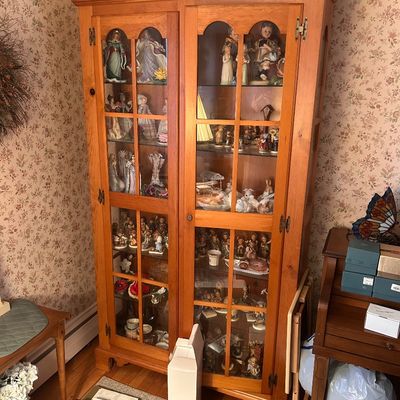 Sale Photo Thumbnail #10: A tall light oak wooden display cabinet filled with collectible porcelain figurines and decorative items.