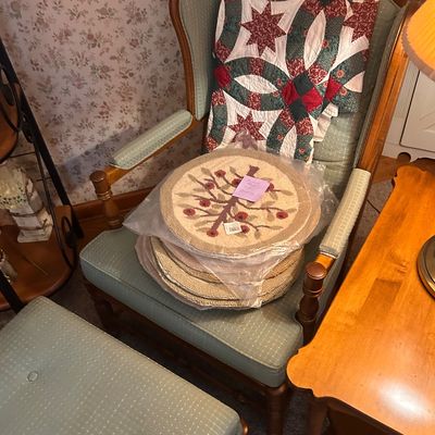 Sale Photo Thumbnail #131: Traditional wooden high-back armchair with green patterned upholstery, matching ottoman, a handmade star and double wedding ring pattern quilt, and a set of round floral hooked placemats.