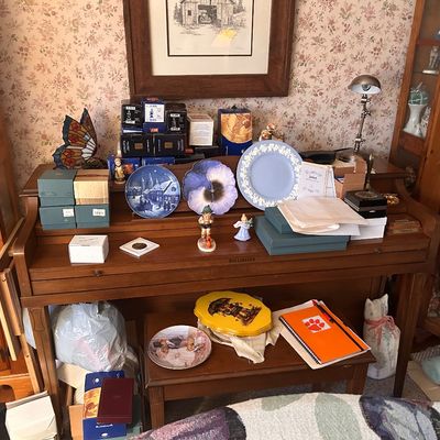 Sale Photo Thumbnail #110: A vintage wooden spinet piano displayed with collectible plates, figurines, boxes, and home decor items.