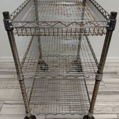 Sale Photo Thumbnail #424: This is a three-tier chrome wire utility rolling cart with a push handle and caster wheels. There is age related wear, including some surface rust. Measurement: 34”L x 18”W x 34”H (approximate). [GG]