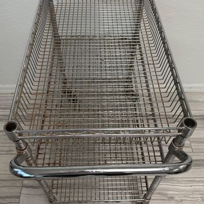Sale Photo Thumbnail #426: This is a three-tier chrome wire utility rolling cart with a push handle and caster wheels. There is age related wear, including some surface rust. Measurement: 34”L x 18”W x 34”H (approximate). [GG]