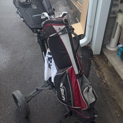 Sale Photo Thumbnail #45: A 3-wheel Tour Trek folding golf push cart equipped with a red, black, and silver Intech golf stand/cart bag. Includes a few golf clubs in the bag as visible. The cart features a drink holder and accessory tray on the handle. Items show signs of outdoor u
