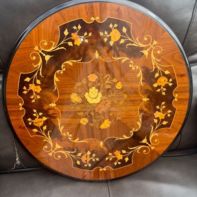Sale Photo Thumbnail #46: Round wooden tabletop or plaque featuring intricate floral marquetry inlay and a high-gloss finish. Displays vibrant botanical motifs in contrasting wood veneers with a scrollwork border. Appears to be in good condition with minor surface wear. Base or le