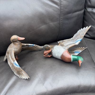Sale Photo Thumbnail #61: Pair of detailed, hand-painted waterfowl duck figurines featuring spread wings and vibrant blue feather accents on wings. Includes one mallard drake with green head and one hen/drake in flight pose. Good pre-owned condition with light surface wear.