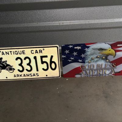 Sale Photo Thumbnail #85: Pair of novelty/decorative license plates. Includes one embossed metal Arkansas Antique Car license plate (number 33156) with vintage vehicle graphic and reflective cream finish, and one novelty front plate featuring a bald eagle with American flag design