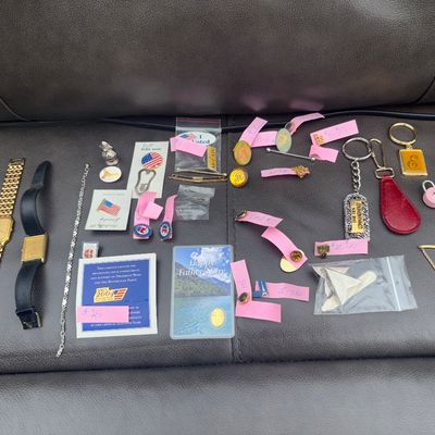 Sale Photo Thumbnail #52: An assortment of vintage jewelry and accessories. Includes two wristwatches (one gold-tone with metal link band, one gold-tone with black leather strap), a fine metal chain, various lapel and enamel pins (including political and USA flag pins), keychains,