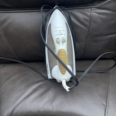 Sale Photo Thumbnail #60: White and grey Black & Decker electric steam iron with tan grip accent. Features variable steam control and spray/burst buttons. Shows light signs of prior use with some wear on buttons. Cord attached.