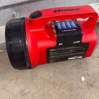 Sale Photo Thumbnail #82: Dorcy brand red molded plastic handheld 6V LED flashlight / lantern. Includes 4 AA batteries stored in the top compartment under the original packaging band. Appears in like-new or unused condition.