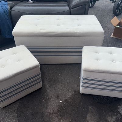 Sale Photo Thumbnail #73: A set of three modern upholstered storage ottomans featuring off-white/cream fabric with blue ticking stripes along the base and button-tufted tops. Includes one large rectangular storage bench and two matching square ottomans. Show light surface wear and