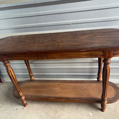 Sale Photo Thumbnail #64: 48X15X26in. A traditional-style oval sofa or console table crafted from wood with turned legs and decorative fluting. Features a starburst-patterned wood veneer top and a lower shelf with woven cane inset. Shows light surface wear, dust, and minor scuffs 