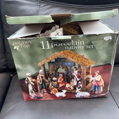 Sale Photo Thumbnail #53: Holiday Time 11-piece hand painted porcelain nativity set in original packaging. Includes nativity scene figurines and creche structure. Outer box shows wear and tearing along the top flaps and edges.