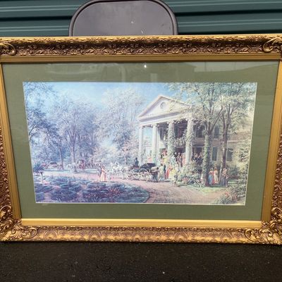 Sale Photo Thumbnail #44: Large framed art print depicting a historical farm wedding scene with figures in period attire and horse-drawn carriages outside a grand columned home. Housed in a heavy, ornate gilt-style molded frame with a green mat border. Shows minor wear to frame ed