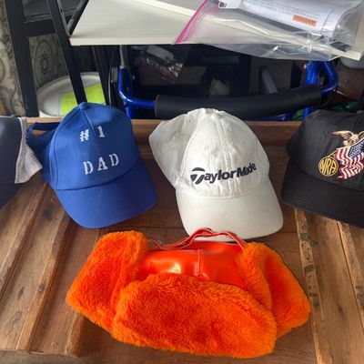 Sale Photo Thumbnail #71: Collection of 5 various mens hats and caps including a navy blue Yeti Coolers mesh trucker hat, a blue '#1 Dad' hat, a white TaylorMade golf hat, a black NRA embroidered baseball cap, and a bright orange faux-fur lined winter trapper hat. Items show light