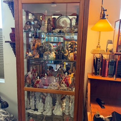 Sale Photo Thumbnail #17: Tall wooden curio display cabinet with glass door and shelves, filled with an extensive collection of Asian porcelain figurines, Japanese Hina dolls, and collectibles.