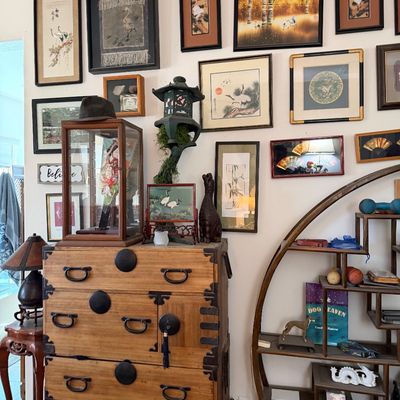 Sale Photo Thumbnail #4: Collection of Asian-inspired home decor including a wooden tansu chest, circular open display shelf, and gallery wall of framed crane artwork.