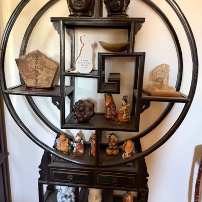 Sale Photo Thumbnail #20: Vintage Asian-style circular shadow box display shelf unit, filled with various Buddha heads, figurines, and decorative artifacts.