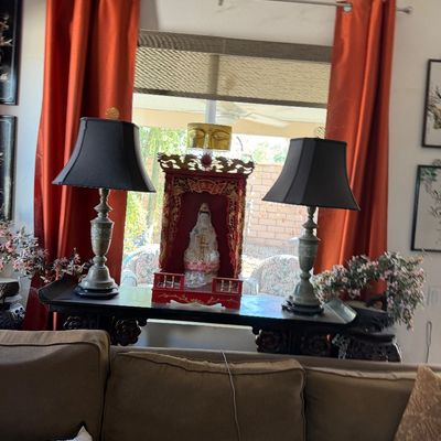 Sale Photo Thumbnail #6: Traditional Asian ornate red and gold altarpiece housing a Guanyin statue, flanked by a pair of silver-toned table lamps with black shades on a dark wood console table.