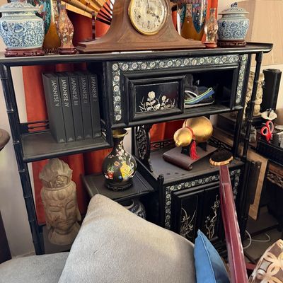 Sale Photo Thumbnail #11: Black lacquer etagere shelf with mother-of-pearl inlay, holding a collection of Asian decor including porcelain vases, a wooden mantel clock, a decorative folding fan, and a Buddha head bust.