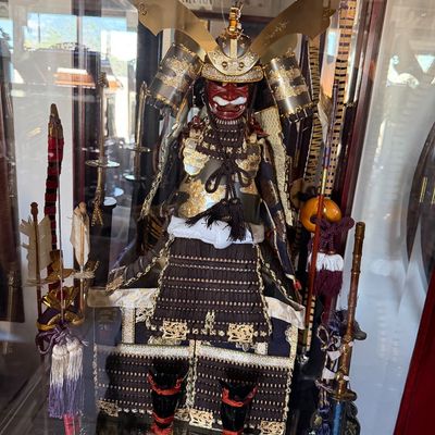 Sale Photo Thumbnail #18: Intricately detailed miniature Japanese samurai armor display set featuring a full suit of armor, helmet, bow, arrows, and swords inside a glass case.