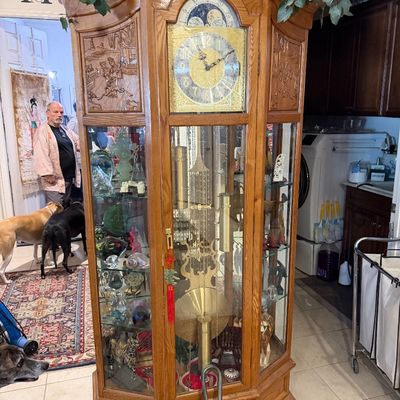 Sale Photo Thumbnail #29: Traditional oak grandfather clock featuring a curio display cabinet with glass shelves and carved wooden side panels.