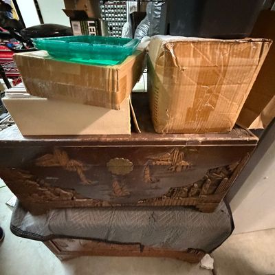 Sale Photo Thumbnail #32: Hand-carved camphor wood chest featuring nautical scenes and brass hardware, stacked with cardboard storage boxes.