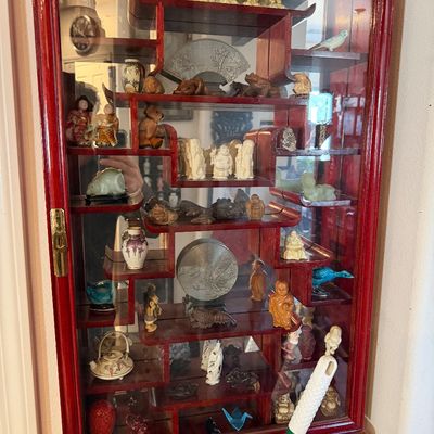 Sale Photo Thumbnail #27: Red-stained wood Asian-style curio display cabinet with tiered shelving, filled with miniature figurines, carvings, and small decorative items.