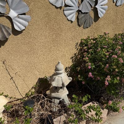 Sale Photo Thumbnail #37: Concrete Japanese-style pagoda garden statue paired with ribbed metal ginkgo leaf wall decor pieces mounted on a stucco exterior wall.