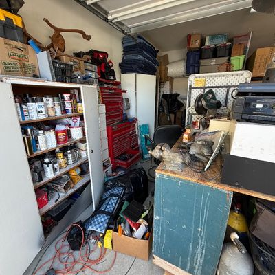 Sale Photo Thumbnail #36: A garage workshop filled with items for sale, including a red metal tool chest, a wooden cabinet stocked with hardware and supplies, workbench tools, moving blankets, and electronics.
