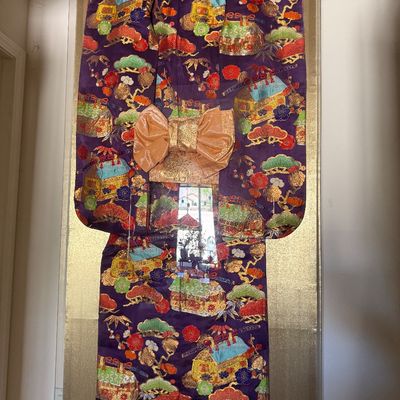Sale Photo Thumbnail #2: Framed vintage Japanese silk kimono displaying vibrant metallic embroidery, colorful motifs, and a metallic gold obi, presented under glass against a golden backing.