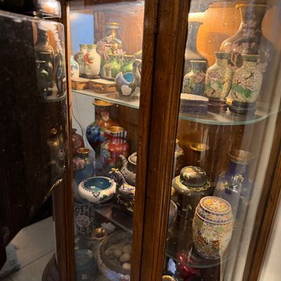 Sale Photo Thumbnail #14: A wooden curio cabinet filled with an extensive collection of Asian cloisonné and enamel decorative items, including vases, jars, and small vessels.