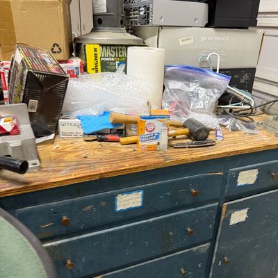 Sale Photo Thumbnail #31: A vintage blue-painted workshop workbench with multiple drawers, topped with an assortment of home improvement supplies, tools, electronics, and household items.