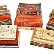 Large collection of vintage books and antique price guides arranged in multiple stacks.