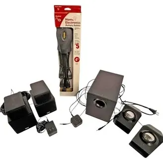 Black computer speaker systems with a subwoofer, satellite speakers, and an in-box multi-outlet extension cord.