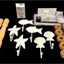 Collection of home decor accessories including white coastal-themed wall hooks, turned wooden table legs, textured gold napkin rings, and...
