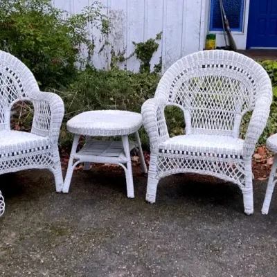 Two white wicker chairs and two end tables and a magazine rack