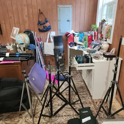 Collection of photography gear including multiple light stands, a tripod, and carrying cases alongside various office items and decor.