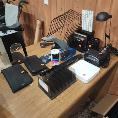 Collection of assorted office supplies arranged on a wooden desk, including staplers, organizers, desk lamps, and an Apple keyboard.