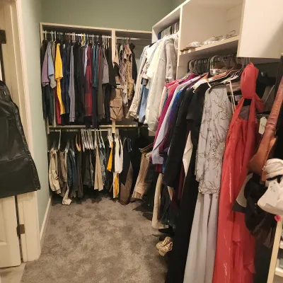 Walk-in closet filled with men's and women's clothing, including casual shirts, pants, outerwear, and formal dresses.