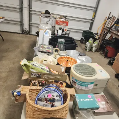 Assorted household and kitchen items on display in a garage, including a Duraflame firestart box, a woven basket with decorative tins, a...