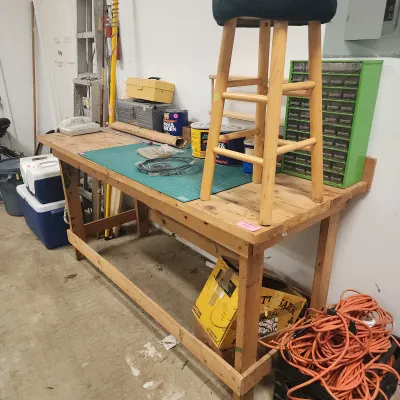 Sale Photo Thumbnail #128: Sturdy handmade wooden workbench with top items including a bar stool, green parts organizer cabinet, cutting mat, and various garage accessories.