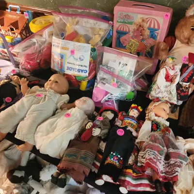 Collection of vintage toys and dolls, including a pink Barbie lunchbox, various ethnic folk dolls, baby dolls, and plastic building toys...