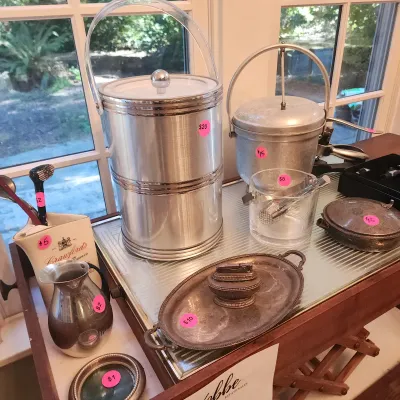 Sale Photo Thumbnail #114: Collection of vintage barware and metal tabletop items, including ice buckets, a silver-plated lighter with tray, small pitcher, and accessories.