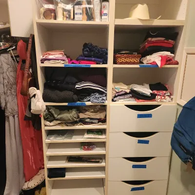 White wooden closet organizer unit filled with folded clothing, accessories, and labeled drawers.