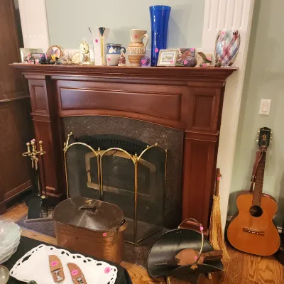 A wooden fireplace mantel featuring various art glass vases, pottery, small collectibles, alongside brass fireplace tools, a metal coal...