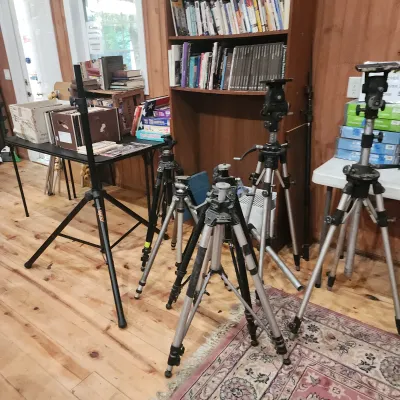 Collection of vintage photography and lighting tripods arranged on a wood floor in front of a bookcase.