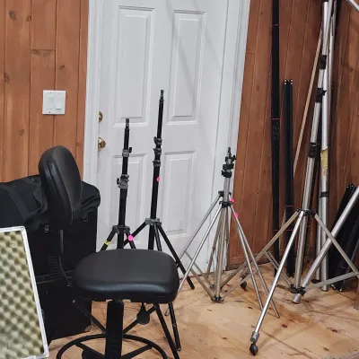 Collection of professional photography equipment, including various light stands, C-stands, and a black padded studio stool.