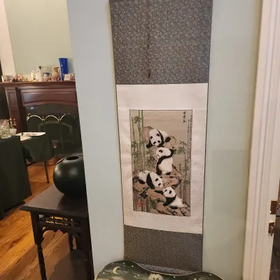 Traditional Chinese hanging scroll painting depicting four pandas playing on rocks surrounded by bamboo.